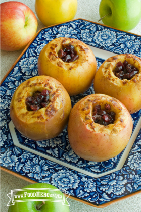 Cuatro manzanas sin corazón rellenas con arándanos rojos, mantequilla y azúcar morena son horneadas, asadas y se muestran en un plato para servir.