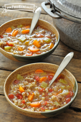 Dos tazones se llenan con una sopa sustanciosa hecha con vegetales, carne molida y cebada.