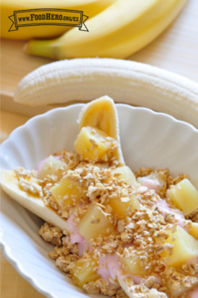 Un tazón con plátano partido por la mitad se cubre con yogur, trozos de piña y una pizca de granola