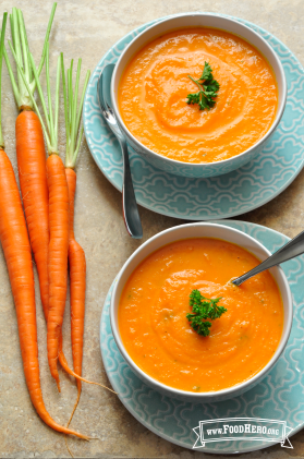 Bowls of smooth carrot soup on serving plates.