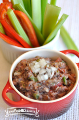 Tazón de cerámica con dip de frijoles servido junto a unos palitos de verduras.  