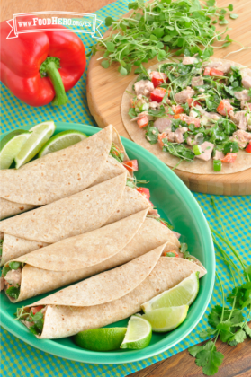 Tortillas dobladas sobre una mezcla cremosa de atún rellena de verduras con rodajas de limón en un plato.