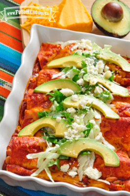 Molde con enchiladas servidas con aguacate, lechuga y queso en el centro.