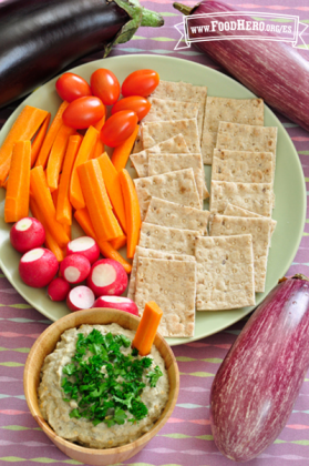 Dip de berenjena adornado con perejil servido con un plato de verduras y galletas saladas.