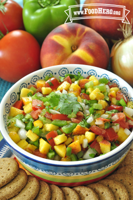 Small bowl of a colorful peach and vegetable salsa shown with crackers.