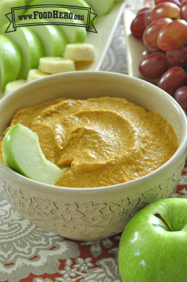 Small bowl of pumpkin dip served with apple slices, banana and grapes.