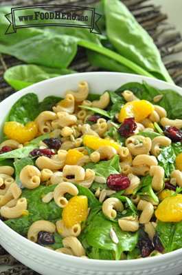 Bowl of a mix of macaroni noodles, spinach, oranges and dried cranberries.