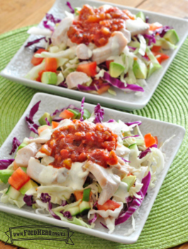 Platos con repollo y verduras debajo de un pescado, aderezo ranchero y salsa.