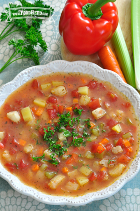 Bowl of soup with cubed vegetables and fish topped with parsley.