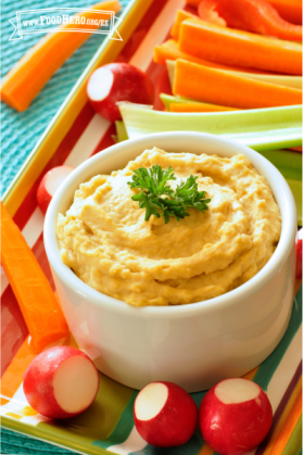 Hummus adornado con perejil servido con palitos de zanahoria, apio y rábanos.