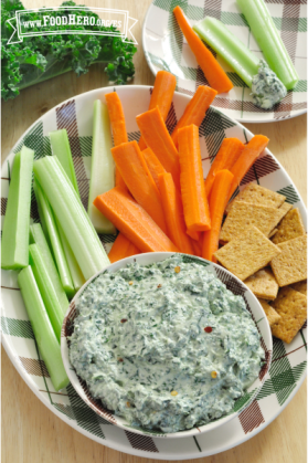 Dip con base de queso cottage y col rizada servido con apio, palitos de zanahoria y galletas saladas.