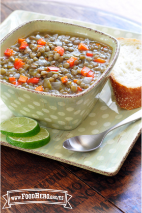 Sopa de lentejas, zanahorias y pimientos dulces servida con limón verde y una rebanada de pan.