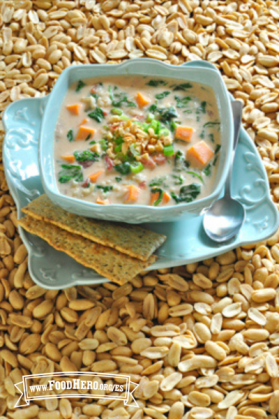 Tazón mediano de sopa de cacahuates y verduras en un plato servido con galletas saladas. 