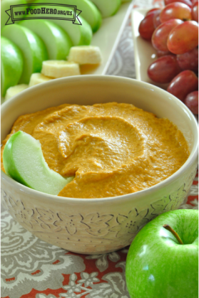 Tazón pequeño de dip de calabaza servido con rodajas de manzana, plátano y uvas.