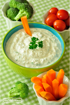 Tazón de dip cremoso adornado con perejil y servido con zanahorias crudas, tomates cherry y brócoli.