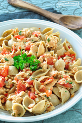 Tazón con pasta con conchas y salmón adornado con perejil.