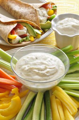 Small bowl of creamy dip with a plate of sliced vegetables and served in a veggie wrap.