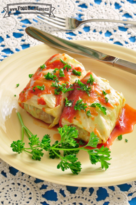 Dos rollitos de repollo bien envueltos y cubiertos con salsa de tomate y guarnición de perejil.