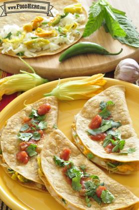 Plate of corn tortillas folded over cheese and squash blossom filling with salsa.