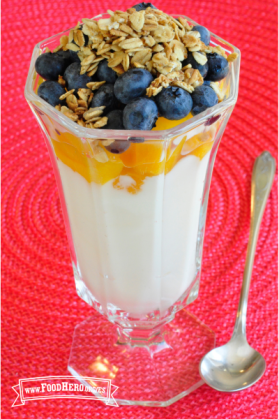 Vaso de cristal con capas de yogur, durazno, arándanos azules y granola.