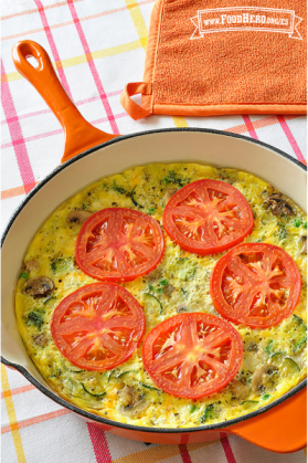 Molde para hornear con una mezcla de verduras y huevo cubierto con rodajas de tomate.