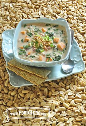 Medium bowl of vegetable and peanut soup on a plate served with crackers.