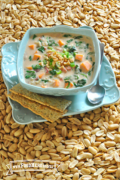 Tazón mediano de sopa de cacahuates y verduras en un plato servido con galletas saladas. 