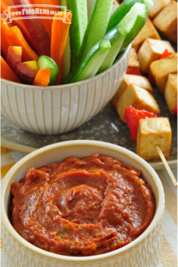 Se muestra un tazón de salsa de plátano y jengibre con tiras de verduras crudas y brochetas de tofu a la parrilla.