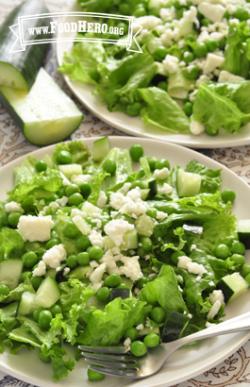 Lettuce bed topped with peas and feta cheese on a plate.