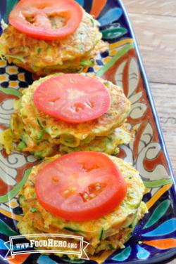 Platter of stacked vegetable patties with a tomato slice. 