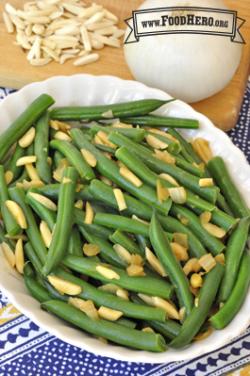 Oval serving dish with tender green beans and toppings. 