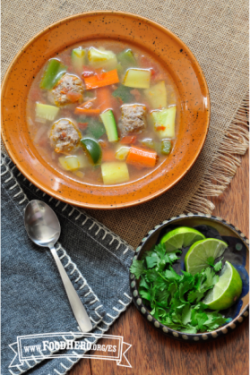 Tazón de sopa de albóndigas, arroz y verduras con limón verde y cilantro.