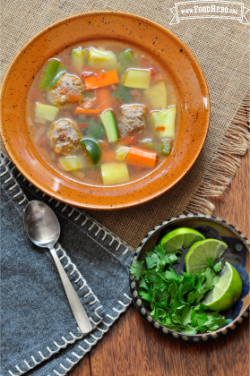 Bowl of meatballs, rice and vegetable soup served with lime and cilantro. 