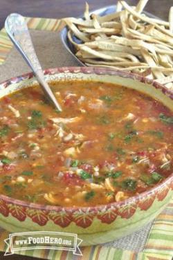 Tomato-based chicken soup in a large bowl with a side of tortilla strips.