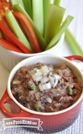 Ceramic bowl with bean dip served next to vegetable slices.