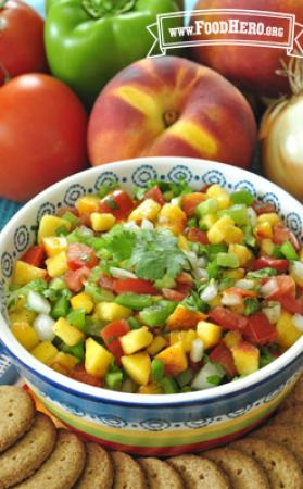 Small bowl of a colorful peach and vegetable salsa shown with crackers.