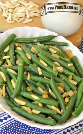 Oval serving dish with tender green beans and toppings. 