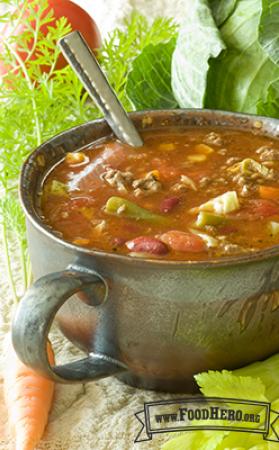 Bowl of soup with a tomato base, vegetables and ground meat.